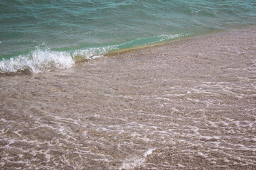 Background of a sandy beach with sea waves. Foam from a wave on the sand. A foamy ocean wave on a seashell beach