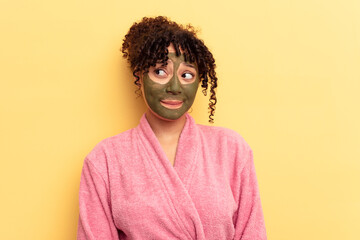 Fototapeta na wymiar Young mixed race wearing facial mask isolated on yellow background confused, feels doubtful and unsure.