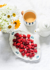 Cup of green tea, fresh ripe raspberries, bouquet of summer flowers on a light background, top view