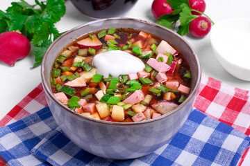 Russian cold soup Okroshka with vegetables, sausage, eggs and kvass topped with sour cream in the bowl 