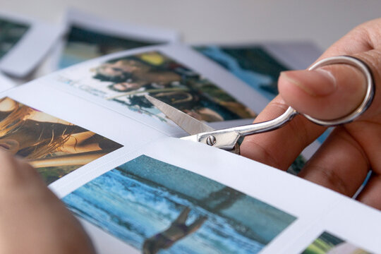 A man cuts out photos with people in close-up. A man uses scissors to cut printed polaroid photos for an album. A person holds a polaroid photo in his hands against the background of other photos.