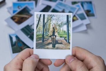 A person holds a polaroid photo in his hands against the background of other photos. Photo in hand...