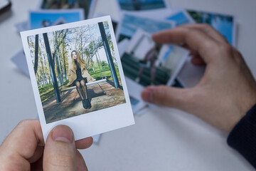 A person holds a polaroid photo in his hands against the background of other photos. Photo in hand...