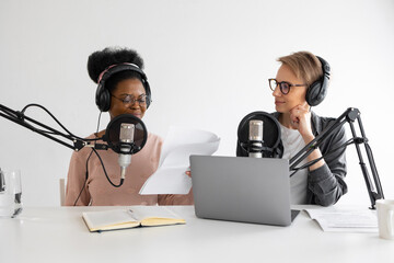 Podcasters, African American and European woman with headphones and microphone recording a podcast...