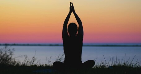 Girl's silhouette sitting in yoga asana at the sea bank on the gradient sunset