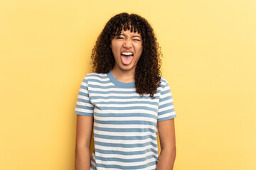 Young mixed race woman isolated on yellow background funny and friendly sticking out tongue.