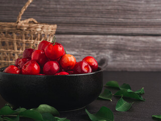 Close-up of red acerola cherries fruit in a ceramic bowl with wooden wall background. High vitamin C and antioxidant fruits. Side view. Concept of healthy fruits