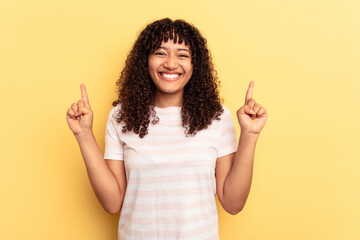 Young mixed race woman isolated on yellow background indicates with both fore fingers up showing a blank space.