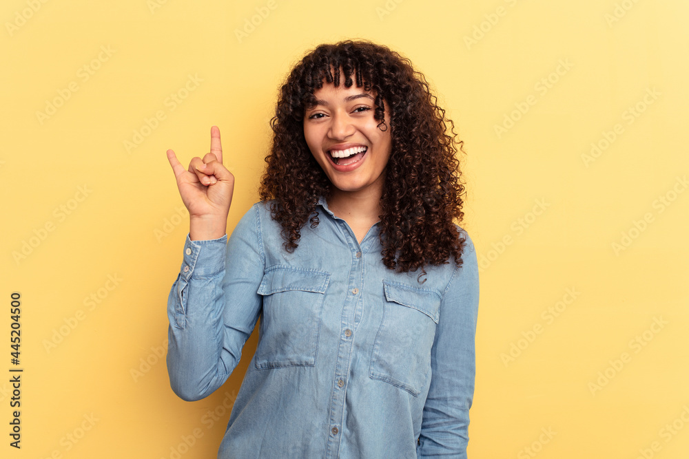 Wall mural Young mixed race woman isolated on yellow background showing a horns gesture as a revolution concept.