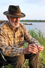 senior male in checkered shirt put the bait of the worm on hook of fishing rod, in nature countryside on lake. fishing hobby, leisure, activity concept