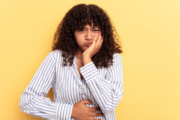 Young mixed race woman isolated on yellow background blows cheeks, has tired expression. Facial...