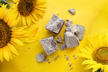 Pieces of Halva and sunflower around it on yellow background. Bright poster with traditional oriental dessert and it ingredient. Top view.