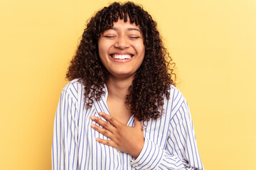 Young mixed race woman isolated on yellow background laughs out loudly keeping hand on chest.