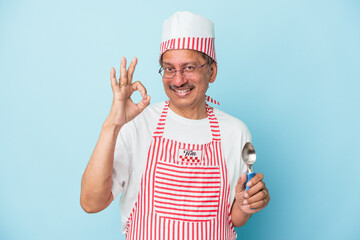 Senior indian ice cream man holding a scoop isolated on blue background cheerful and confident...