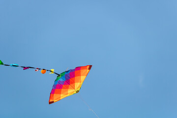 Child's rainbow coloured diamond kite with tail flying high in clear blue summer sky