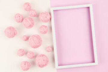 A white empty frame and a lot of pink balls of yarn for knitting or crocheting on a white and pink...