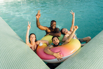Four multiracial friends with a float in the pool, having fun in summer.