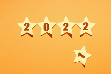 Paper stars from 2022 and discarded star with number 1 on yellow background, new year greetings.