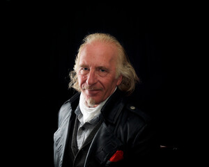 Obraz premium Studio portrait of adult male long haired steampunk wearing black leather and white silk cravat against black background, side lighting