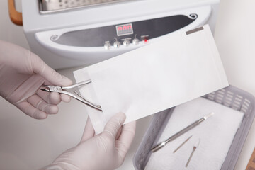 Unrecognizable manicurist putting nail nippers in paper envelope for dry heat sterilization