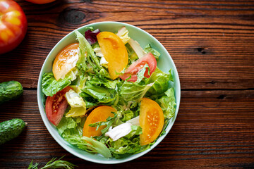 Healthy salad of fresh vegetables, herbs and tomatoes on a wooden background.
