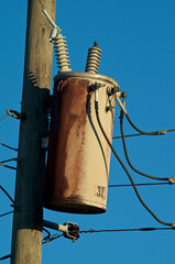 An old tan colored rusted electrical transformer on wood pole against blue sky