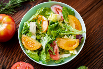 Healthy salad of fresh vegetables, herbs and tomatoes on a wooden background.