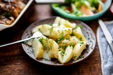 Boiled young potatoes with dill, fresh vegetable salad and baked chicken thighs on a dark wooden background.