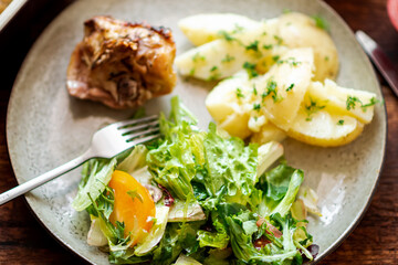 Boiled young potatoes with dill, fresh vegetable salad and baked chicken thighs on a dark wooden background.