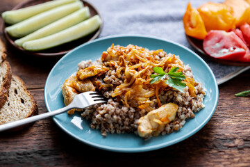 Buckwheat porridge with meat, onions and carrots on a wooden background. With fresh vegetables, cucumbers and tomatoes.