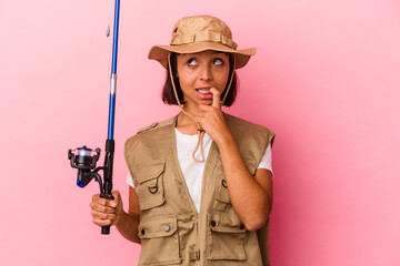 Fototapeta premium Young mixed race fisherwoman holding a rod isolated on pink background relaxed thinking about something looking at a copy space.
