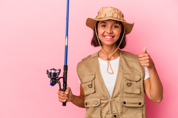Young mixed race fisherwoman holding a rod isolated on pink background smiling and raising thumb up