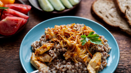 Buckwheat porridge with meat, onions and carrots on a wooden background. With fresh vegetables, cucumbers and tomatoes.
