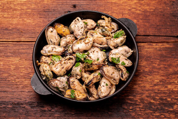 Peeled mussels in sauce on a dark wooden background.