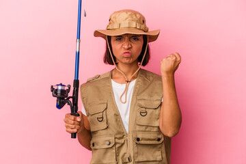 Young mixed race fisherwoman holding a rod isolated on pink background showing fist to camera, aggressive facial expression.