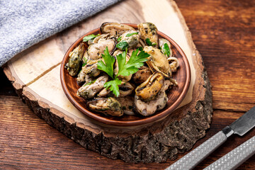 Peeled mussels in sauce on a dark wooden background.