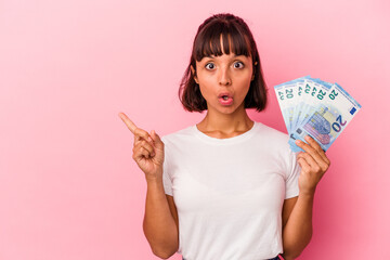 Young mixed race woman holding bills isolated on pink background pointing to the side