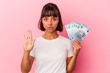 Young mixed race woman holding bills isolated on pink background standing with outstretched hand showing stop sign, preventing you.