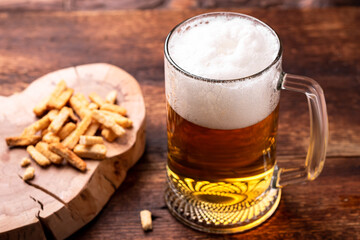 Glass of beer and snacks on a wooden background.
