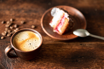 Cup of coffee and a piece of cake on a dark wooden background.