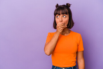 Young mixed race woman isolated on purple background thoughtful looking to a copy space covering mouth with hand.