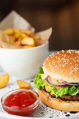 Close-up of tasty burger with salad cheese and sauce, fried potatoes and kethcup