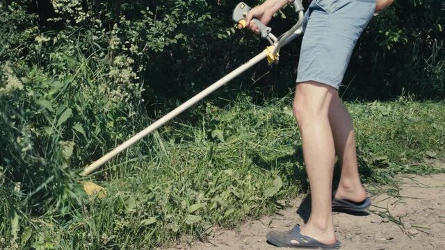 Amateur man cutting grass by petrol brushcutter or grass trimmer with star-shaped three steel knife blades and grass deflector. Garden or agricultural tool used to trim weeds. Hand held brush cutter
