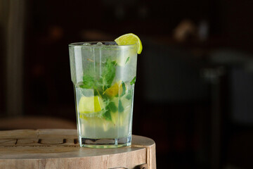 Refreshing summer cocktail mojito with ice, fresh mint and lime. Mojito cocktail on a dark background. Wooden stand.