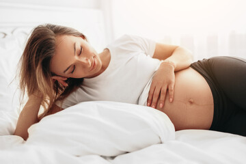 Obraz na płótnie Canvas Dreamy pregnant woman touching belly in bed