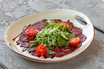 Beef carpaccio with arugula and parmesan on gray surface