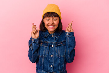 Young mixed race woman isolated on pink background crossing fingers for having luck