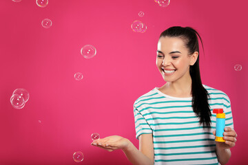 Young woman having fun with soap bubbles on pink background, space for text