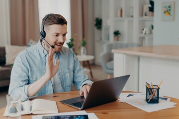 Happy Caucasian guy waving hand during video call to colleague