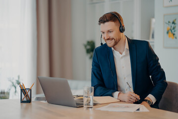 Smiling glad successful businessman practices online conference has distance meeting with...